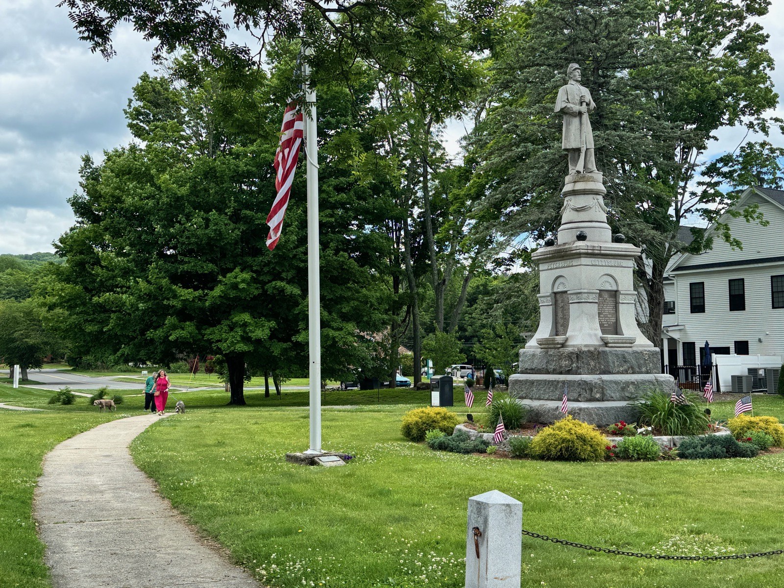 A monument, flag, walkway, mature trees, and nearby building in Wilbraham Center